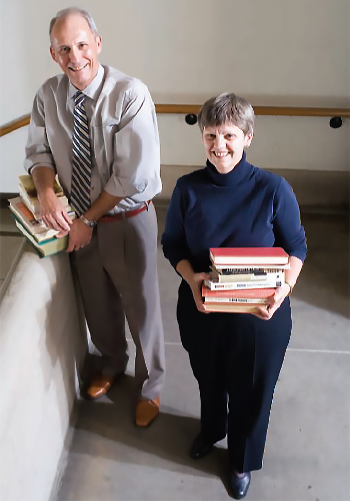 Jim and Verna Webb, standing on a stair landing, each holding a pile of books