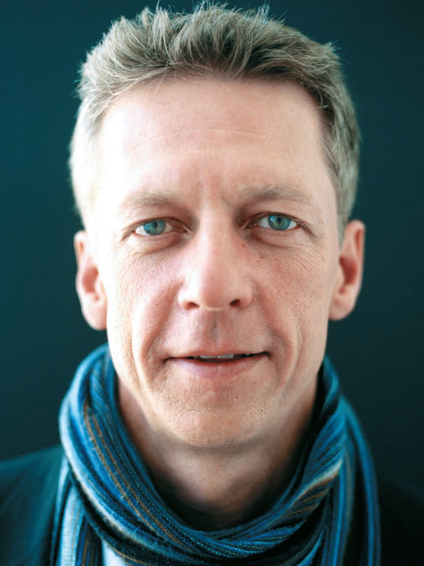 Close-up headshot of Dr. James Orbinski, wearing a blue-striped scarf, against a dark grey background