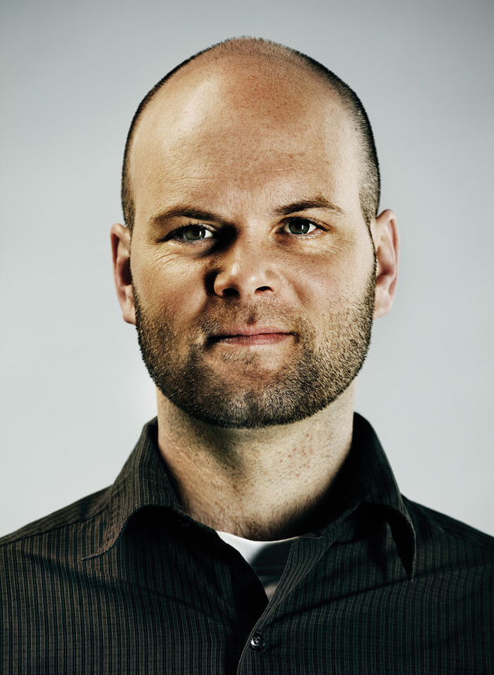 Headshot of Kieran Hayward, wearing a black collared, button-up shirt