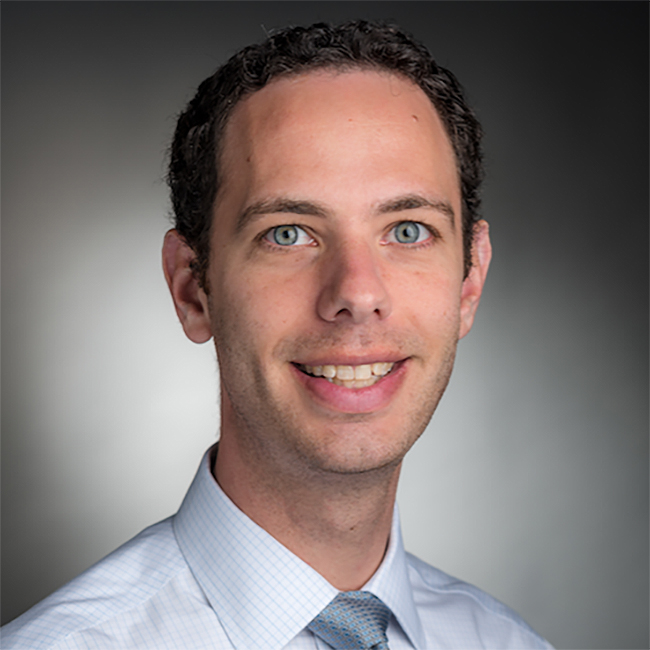 Headshot of Michael Goldberg, wearing a white collared shirt and striped tie