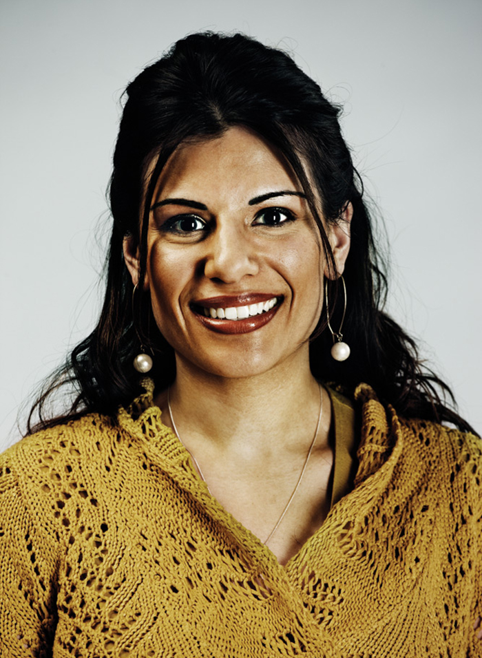 Headshot of Preena Chauhan, wearing pearl hooped earrings and a mustard-coloured lace knit sweater