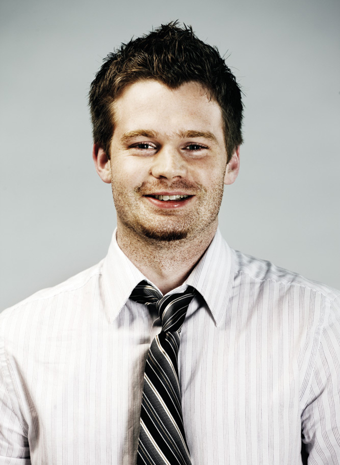 Headshot of Stephen Tracy wearing a white long-sleeved collared shirt and a black, grey and white striped tie