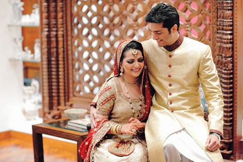 Mehreen and Arsalan Rashid, wearing traditional Pakistani wedding clothes, smiling and sitting close together, with Arsalan's arm around Mehreen