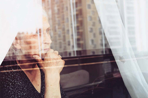 Photo of an elderly woman looking pensively out a window.