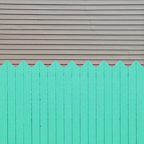 Photo of light grey horizontal lines in the upper half and light green, vertically lined picket fence in the bottom half