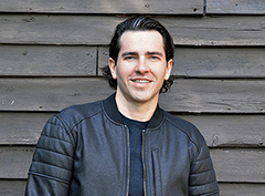 Close-up photo of Brendan Bowles standing against the side of a wooden building