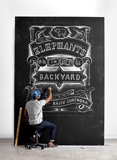 Photo of Rajiv Surendra drawing the cover of "The Elephants in My Backyard" on a large chalkboard