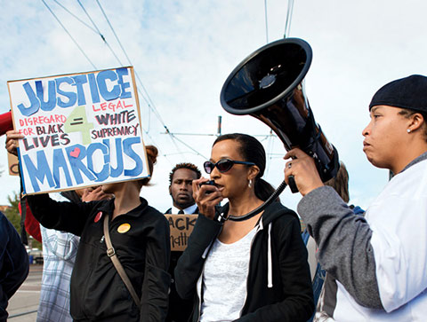 Photo of a group of protesters, one speaking through a loudspeaker and one holding a sign (