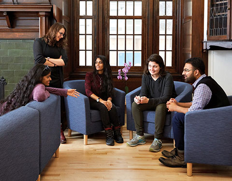 Photo of students seated in armchairs and conversing in the School of Graduate Studies' student lounge