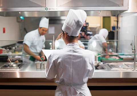 Backup member Ailin Xi overlooking U of T's Iron Chef team while they are working in the kitchen