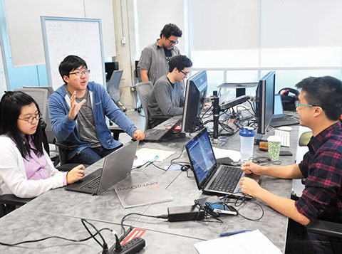 Photo of students collaborating at a table and working with laptops in the Hub.