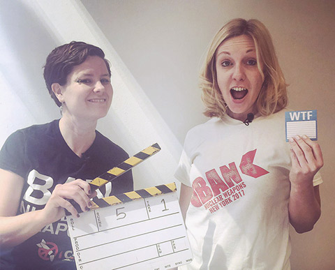 Ray Acheson holding a movie clapboard and Allison Pytlak holding a tag with the letters 