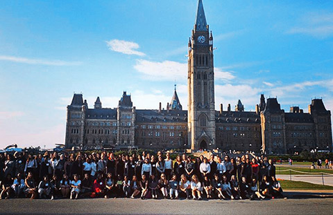 Photo of 100 female U of T students in front of a building on Parliament Hill.