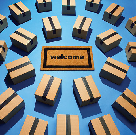 Photo of a welcome mat surrounded by concentric circles of sealed cardboard shipping boxes.