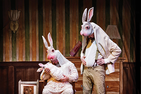 Photo of a scene in Jabberwocky: Ma is sitting in a chair holding her son, and Pa is standing next to her.