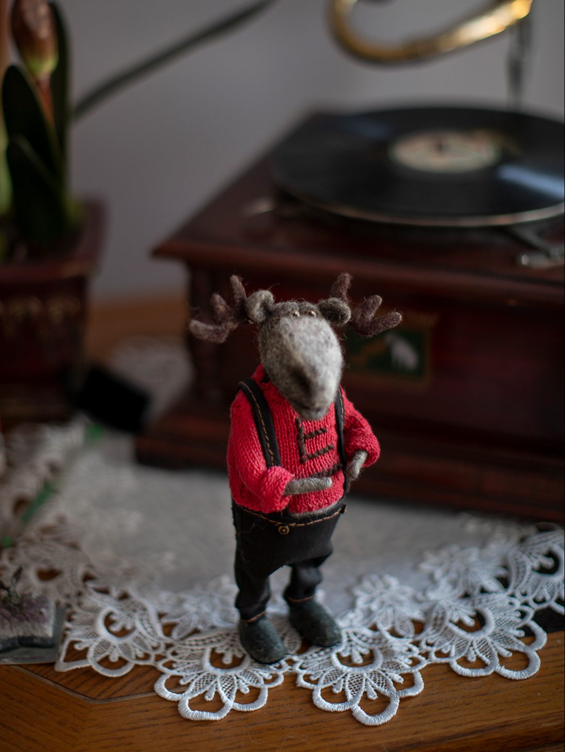 A small moose made out of wool stands on a wooden table next to a gramophone