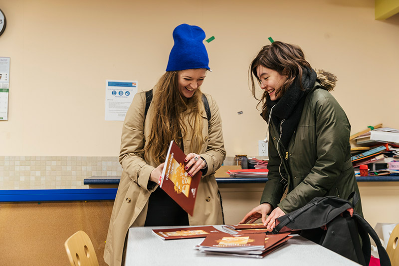 Bahia Marks and Maya Wong are gathering pamphlets and smiling.