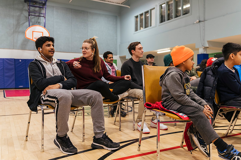 Marks and Gabrial sit together among others in a gymnasium.