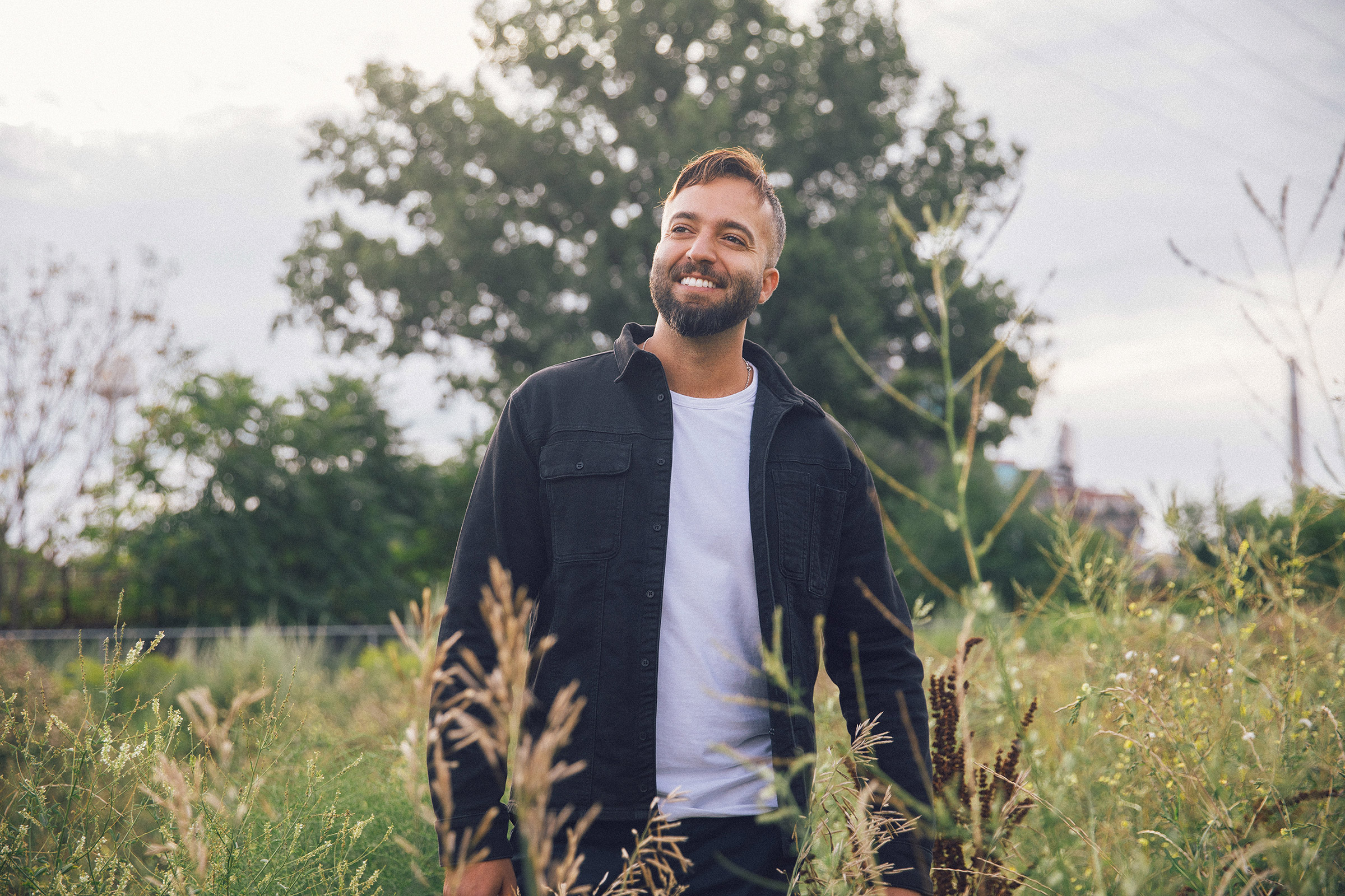 Prof. Fadi Masoud in a white shirt and black jacket, smiling and standing in a field of shrubs