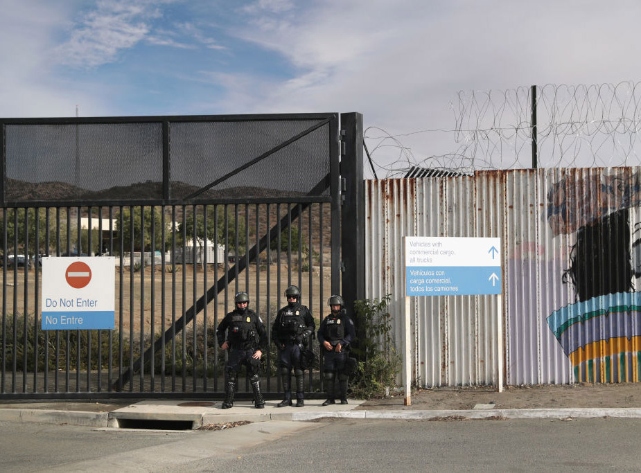 Three U.S. Customs and Border Protection officers stand in front of a gate next to a Do Not Enter sign.