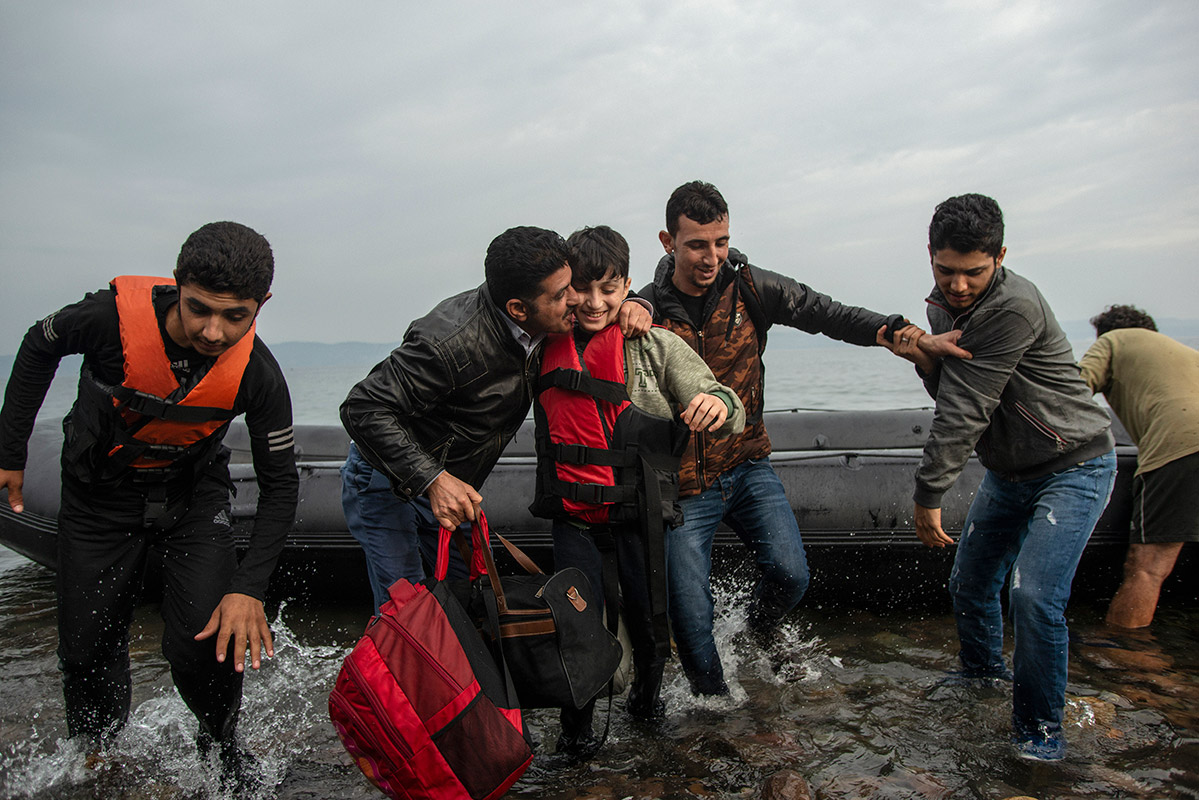 A Syrian refugee boy is kissed by his father after disembarking from a dinghy along with other refugees and migrants at a beach