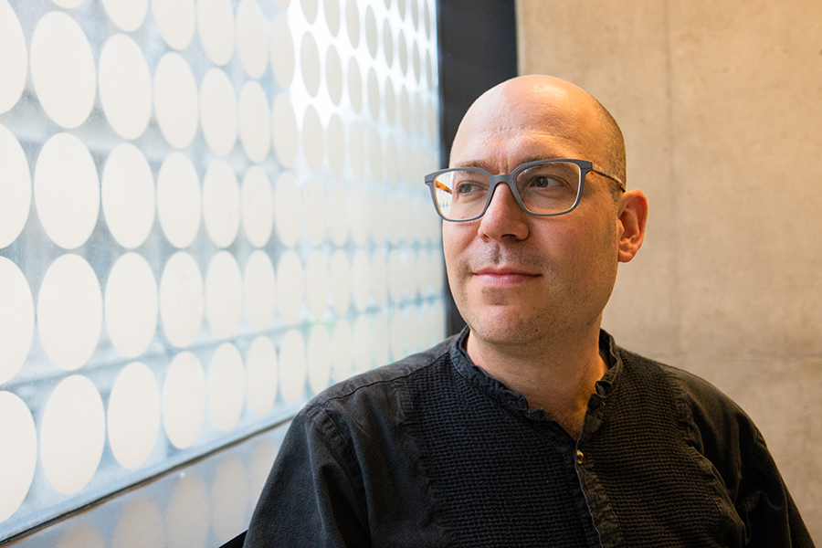 Headshot of Prof. Aspuru-Guzik looking out of a window on the left side of the photo