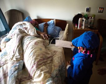 Young child in blue uniform delivering a letter to an elderly woman lying in bed