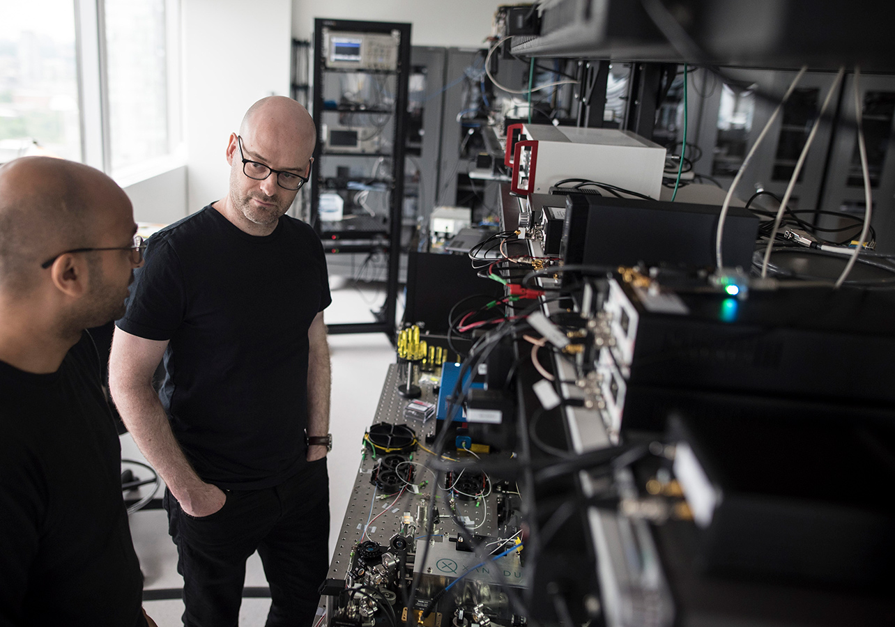 Christian Weedbrook standing in front of quantum computers and listening as Varun Vaidya discusses the working principle of one of the building blocks of quantum computers at their Toronto office