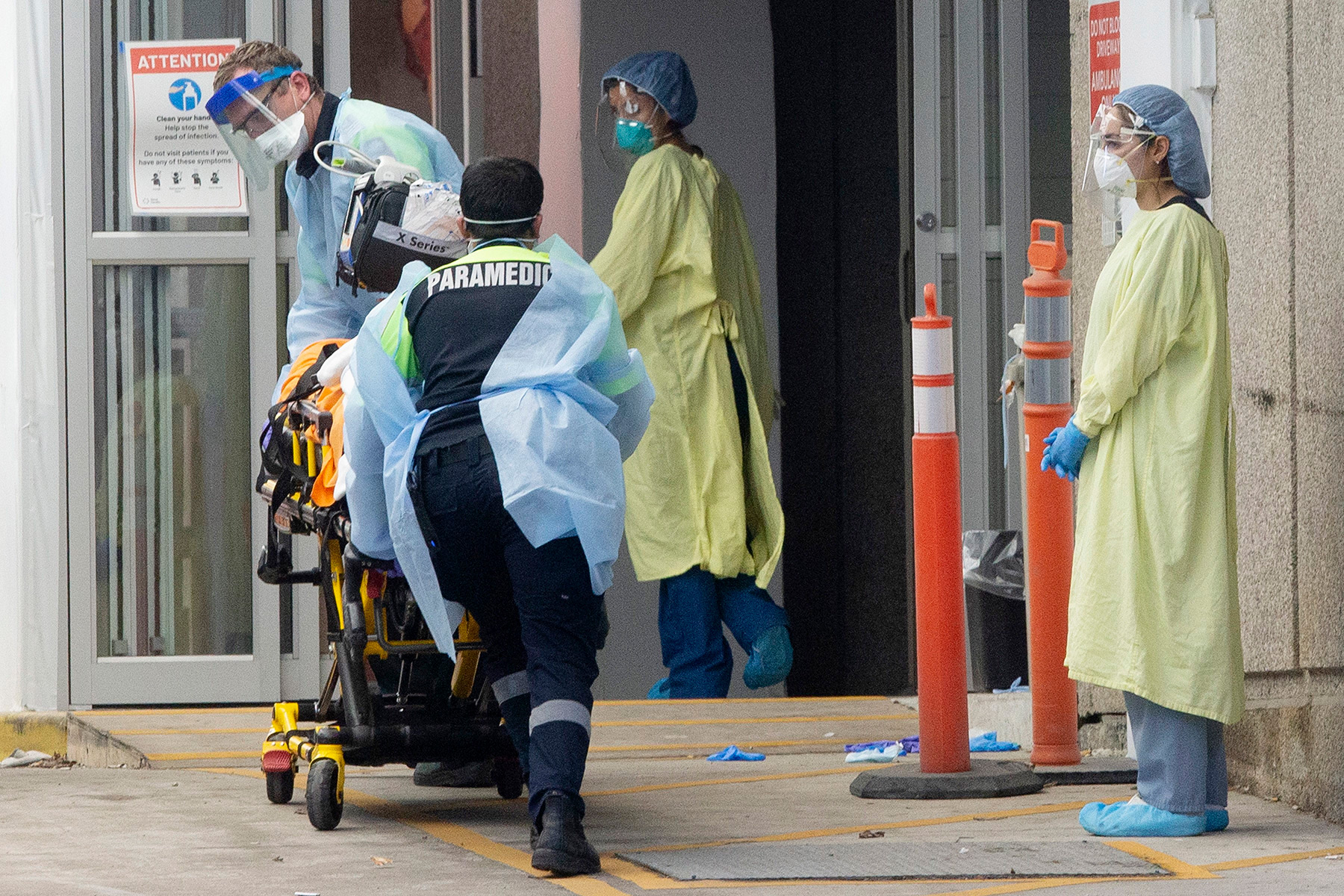 Paramedics wearing protective equipment wheel a patient into a hospital emergency department