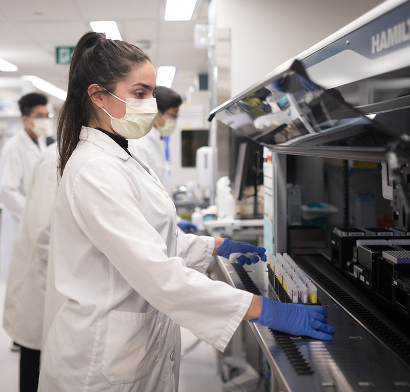 A U of T researcher holding an array of test tubes in front of a machine