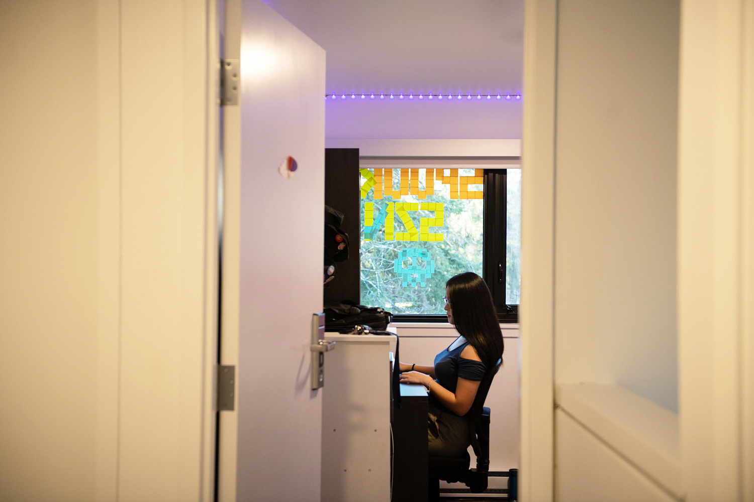 Shirley Liu working on her computer at her desk in her residence room with the door open