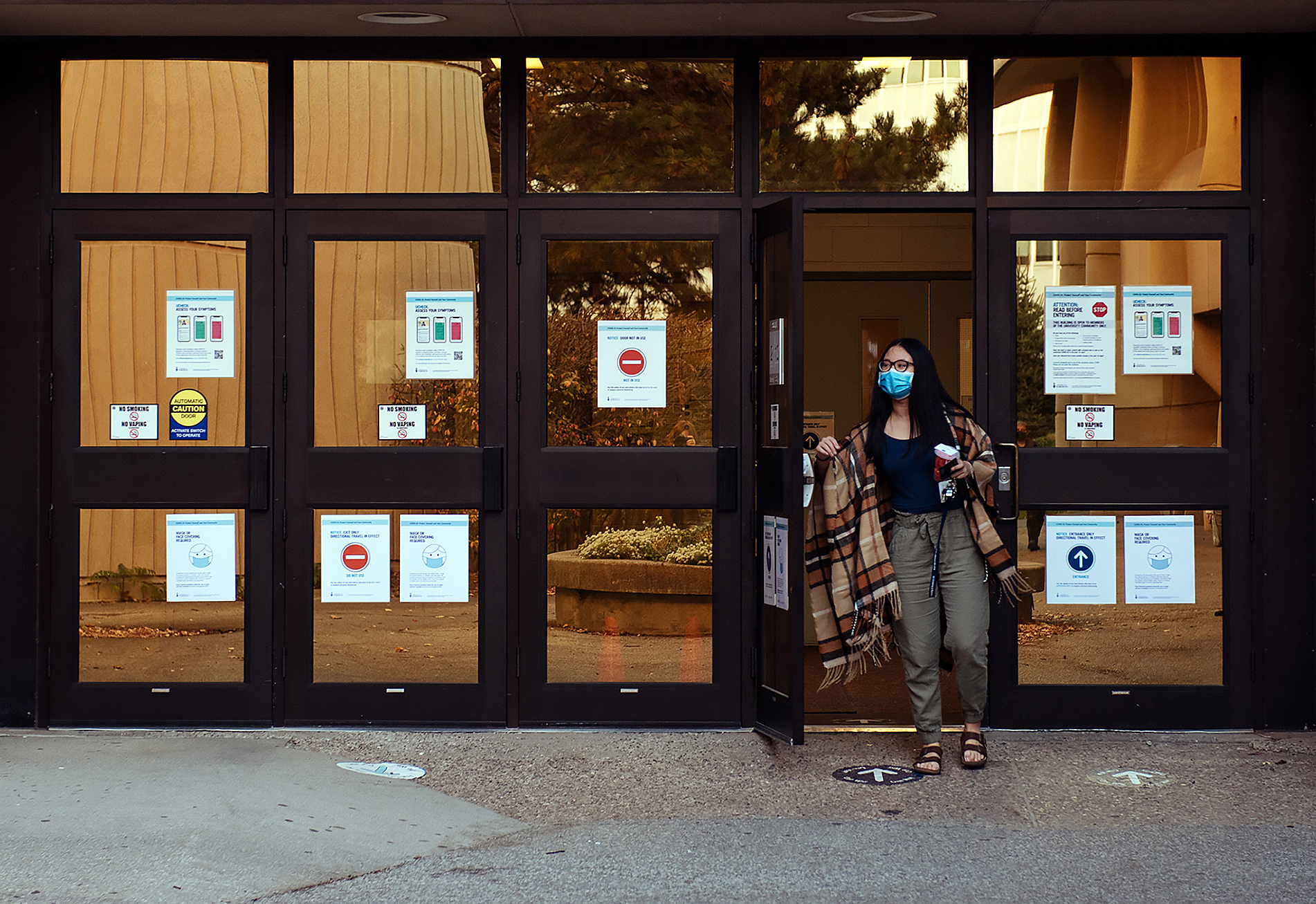 Shirley Liu leaving a building with warning signs on the doors and arrows on the ground indicating direction of foot traffic