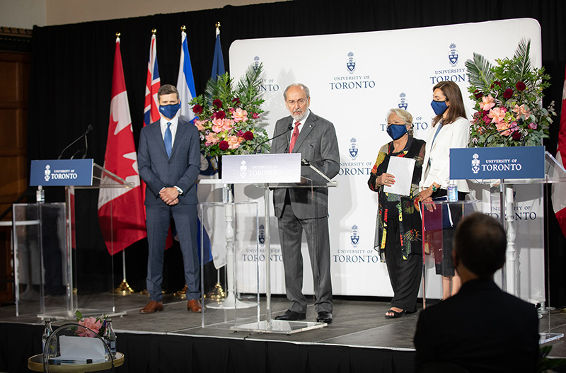 James Temerty speaking in front of a lectern, standing on a podum with three other people