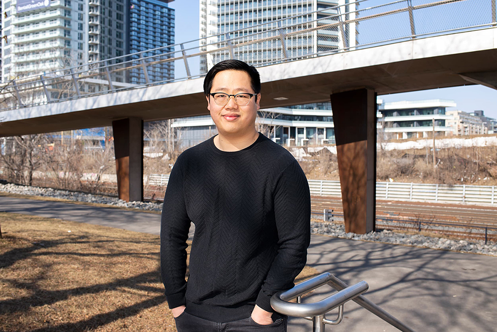 Outdoor photo of Austin Yeh with a bridge and residential buildings in the background