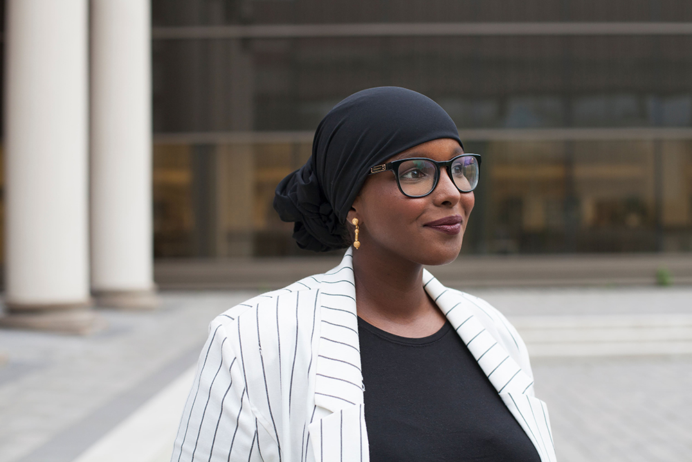 Ikran Jama with hair covered in a black cloth, standing in front of a building