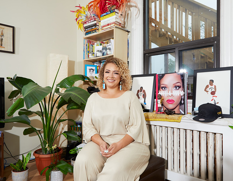 Pacinthe Mattar sitting next to a window next to houseplants and framed pictures, with a bookshelf behind her