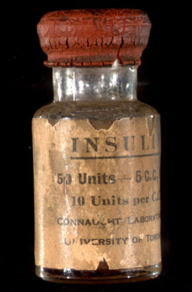 An old vial of insulin with a cracked red stopper and a frayed label that reads "INSULIN 50 Units-5 C.C. 10 Units per C.C. Connaught Laboratories University of Toronto"