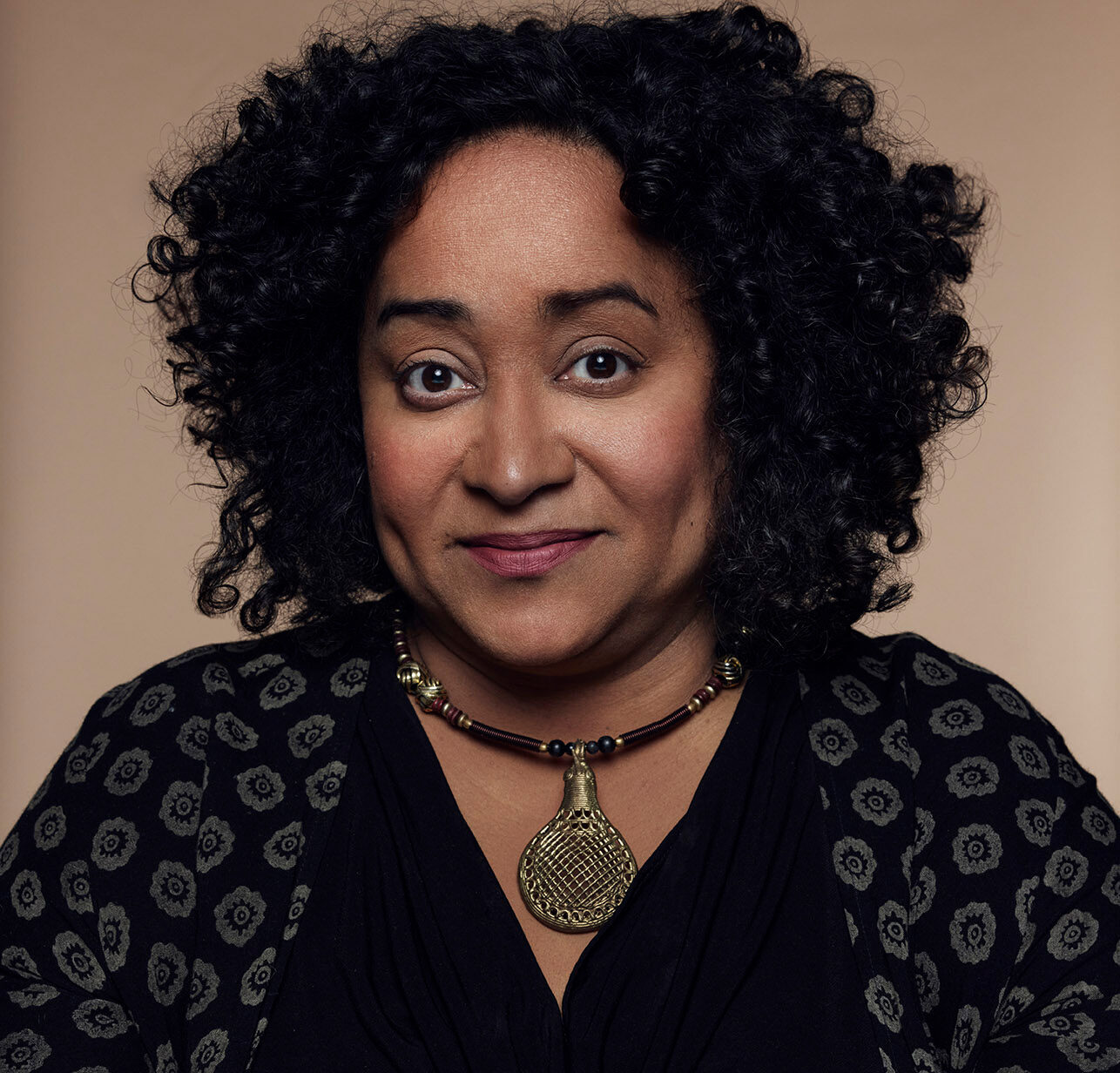 Close up of Prof. Caroline Shenaz Hossein, in a black cardigan with a grey flower pattern, wearing a large bronze pendant