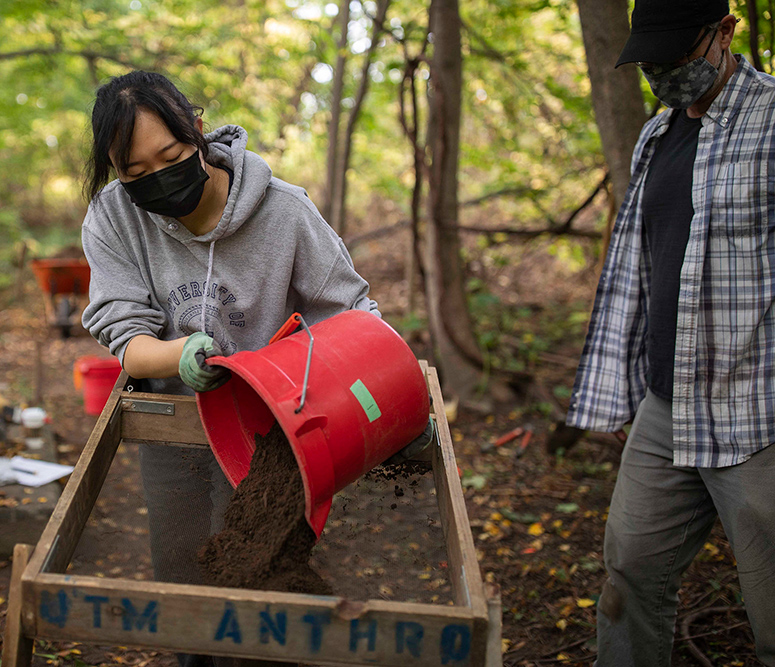 Student pouring dirt from a red pail onto a mesh screen