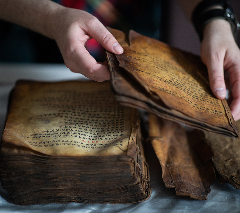 A pair of hands lifting the darkening, fraying pages of an ancient text