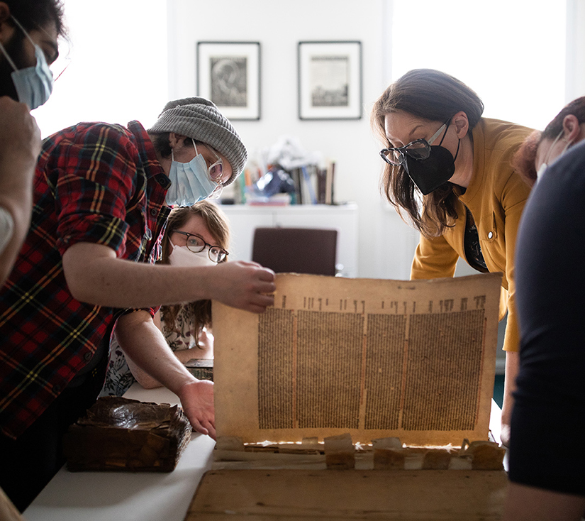 Prof. Alexandra Gillespie and PhD students standing around a table examining an ancient text