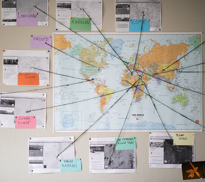 Large world map with different pins on the map connected by string to printouts of maps and images labelled with different city names around the world