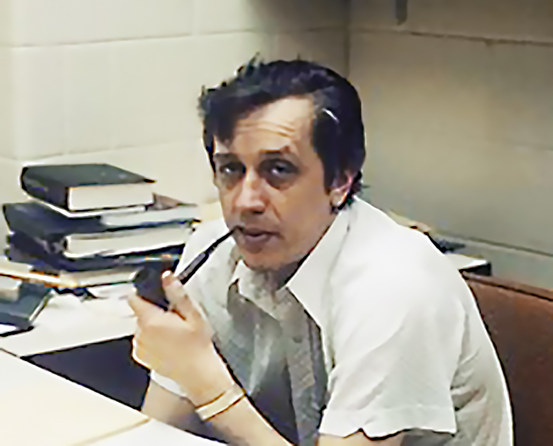 Andrew John Becker sitting at his desk, holding a pipe