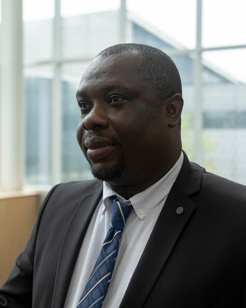 Close up of Dr. Roger Antabe wearing a white shirt, blue patterned tie and dark jacket