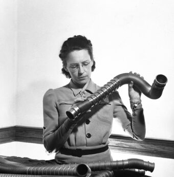 Black and white photo of Elsie MacGill holding and examining a section of a pipe.