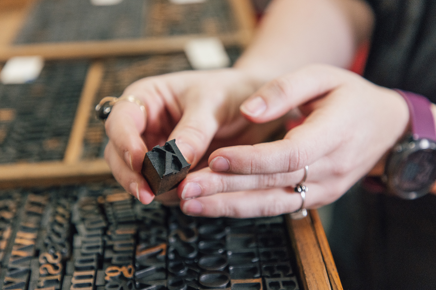 A hand holds a small wooden block of type for the letter K