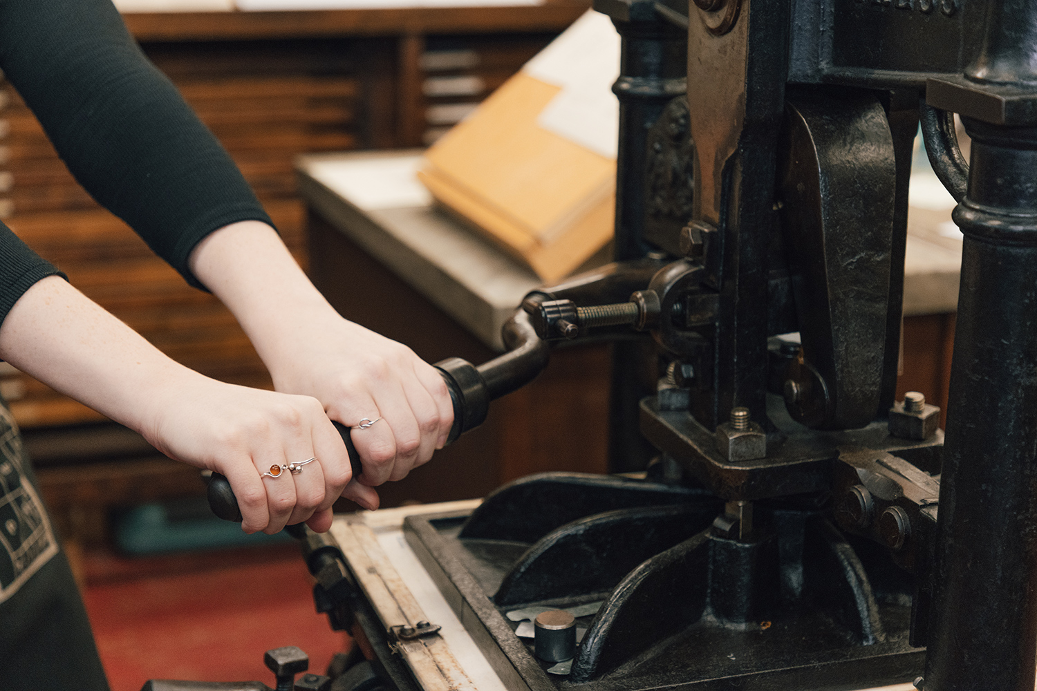 A close-up of two hands pulling on a large lever attached to a black iron press