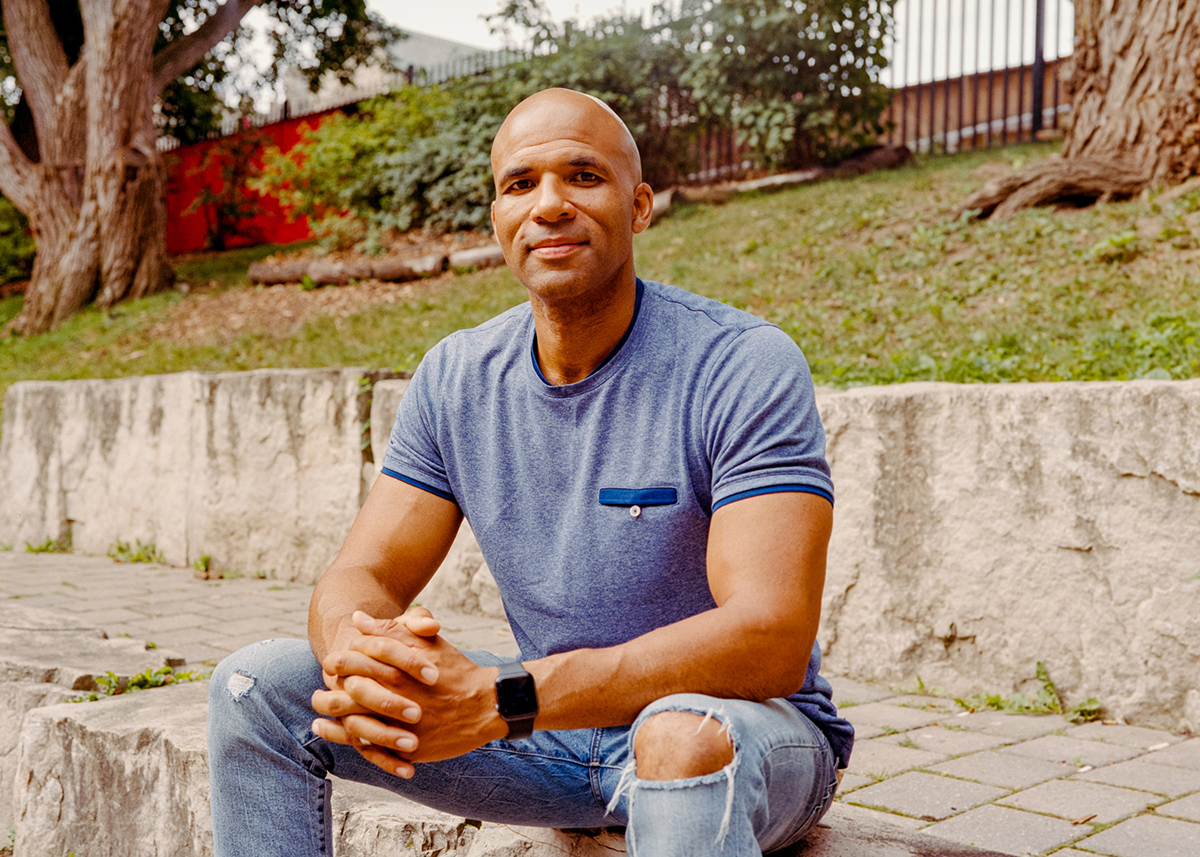 U of T Mississauga professor Akwasi Owusu-Bempah sitting outside in a T-shirt and ripped jeans