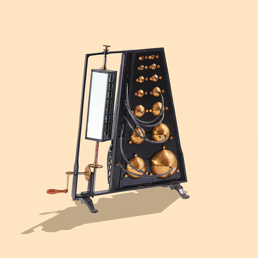 Fourteen brass spherical resonators of increasing size from top to bottom, attached to the right side of a steel frame, which is attached to a rotating mirror on the left side. Rubber hoses are connected to several of the spheres.