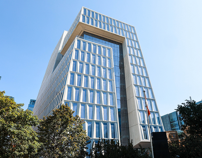 Sunny, exterior view of the west side of the Schwartz Reisman Innovation Campus. The building consists of a tapered tower with narrow windows all around.